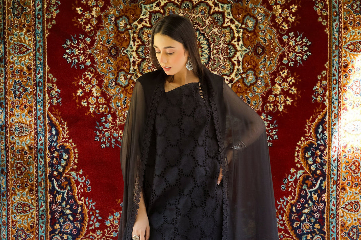 Woman in a black outfit standing in front of a decorative rug with a chandelier above.
