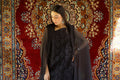 Woman in a black outfit standing in front of a decorative rug with a chandelier above.