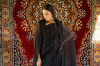 Woman in a black outfit standing in front of a decorative rug with a chandelier above.